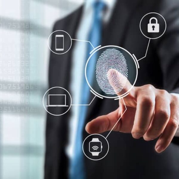 A person in a suit touches a transparent screen displaying a fingerprint icon, which is connected to icons representing a smartphone, laptop, smartwatch, and padlock, symbolizing digital security and multi-device authentication.