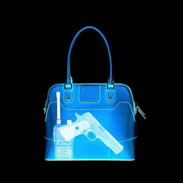 X-ray image of a handbag revealing a pistol and a two-way radio inside. The handbag is shown in blue, highlighting the contents prominently against a black background.